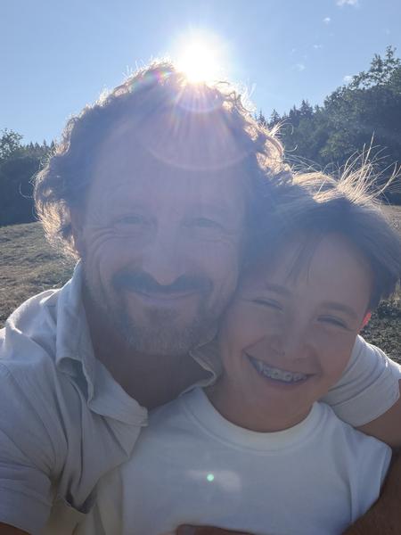 A heartwarming selfie captures two individuals, likely father and child, smiling brightly under a radiant sun